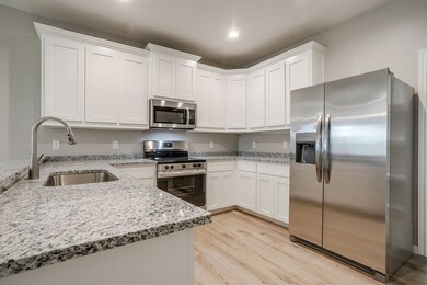 Kitchen featuring stainless steel appliances, light stone counters, white cabinets, and light wood-type flooring