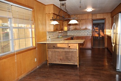 Kitchen with wood walls, brown cabinetry, dark wood-style flooring, freestanding refrigerator, and a peninsula