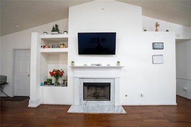 Living room with lofted ceiling, wood finished floors, a high end fireplace, built in shelves, and baseboards