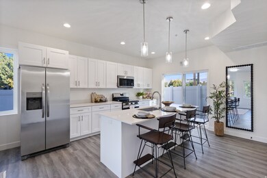 Kitchen with stainless steel appliances, hanging light fixtures, white cabinets, light wood-type flooring, and a kitchen breakfast bar