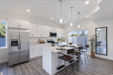 Kitchen with stainless steel appliances, hanging light fixtures, white cabinets, light wood-type flooring, and a kitchen breakfast bar