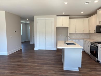 Kitchen with decorative backsplash, stainless steel appliances, light stone counters, an island with sink, and white cabinets