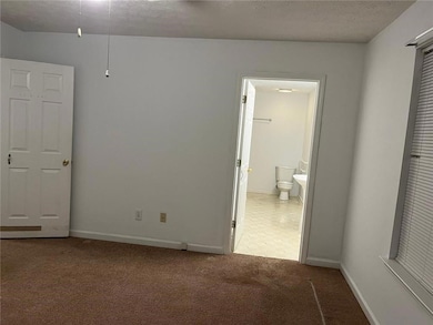 Unfurnished bedroom featuring a textured ceiling, light carpet, and ensuite bath