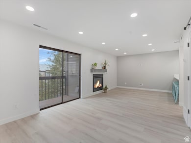Unfurnished living room featuring recessed lighting, light wood-style flooring, a glass covered fireplace, and a barn door
