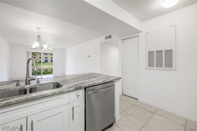 Kitchen with white cabinets, dishwasher, light tile patterned floors, light stone counters, and decorative light fixtures