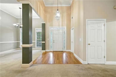 Entryway with carpet flooring, a chandelier, a high ceiling, ornamental molding, and wood finished floors