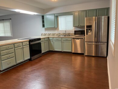 Kitchen featuring stainless steel appliances, dark wood finished floors, light countertops, open shelves, and a peninsula