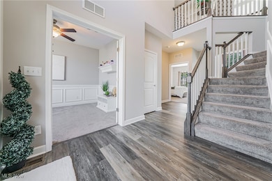 Foyer entrance featuring wood finished floors, stairway, a ceiling fan, wainscoting, and a towering ceiling