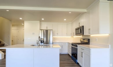 Kitchen with stainless steel appliances, recessed lighting, white cabinets, a center island with sink, and dark wood finished floors