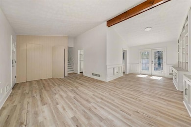 Unfurnished living room featuring french doors, stairs, light wood finished floors, and a decorative wall
