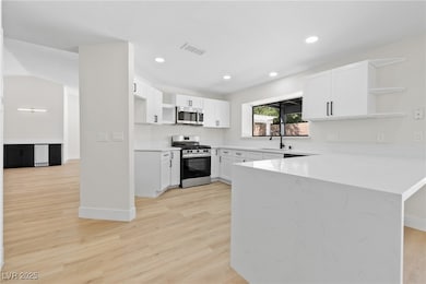 Kitchen with open shelves, white cabinets, appliances with stainless steel finishes, a peninsula, and light stone countertops