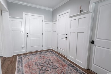 Doorway with crown molding and dark wood-type floo