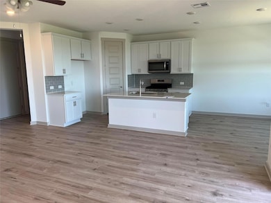 Kitchen with white cabinets, light wood-style flooring, stainless steel appliances, backsplash, and recessed lighting