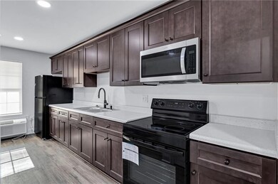 Kitchen with dark brown cabinetry, black appliances, light wood finished floors, recessed lighting, and an AC wall unit