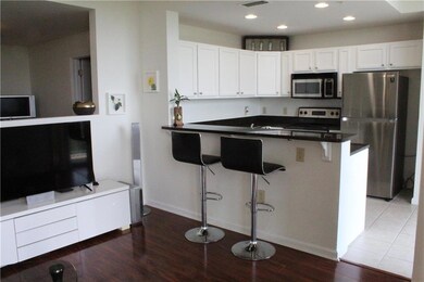 Kitchen featuring stainless steel appliances, wood finished floors, white cabinetry, a peninsula, and dark countertops