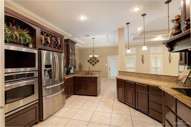 Kitchen with appliances with stainless steel finishes, a sink, ornamental molding, a tray ceiling, and dark brown cabinetry