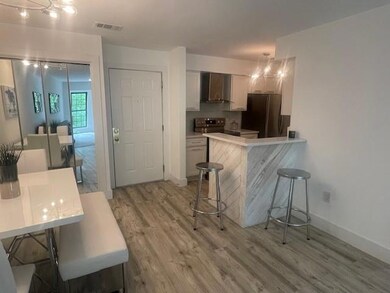 Kitchen featuring a breakfast bar, light wood-type flooring, a peninsula, light countertops, and wall chimney exhaust hood