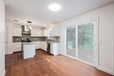 Kitchen with pendant lighting, tasteful backsplash, a textured ceiling, wall chimney exhaust hood, and dark wood-style flooring