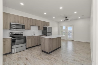 Kitchen featuring appliances with stainless steel finishes, a ceiling fan, light countertops, a center island, and decorative backsplash