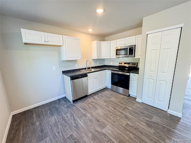 Kitchen featuring white cabinetry, stainless steel appliances, dark countertops, dark wood-style floors, and recessed lighting