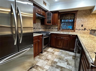 Kitchen with stainless steel appliances, cherry wood cabinetry, tile backsplash, glass insert cabinets, and under cabinet range hood