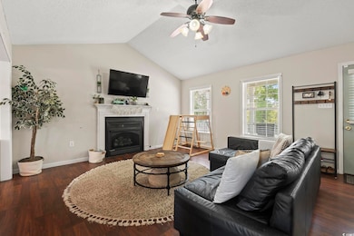 Living room with wood finished floors, ceiling fan, a fireplace, and vaulted ceiling