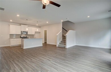 Kitchen featuring open floor plan, dark wood finished floors, white cabinets, a kitchen island with sink, and stainless steel appliances