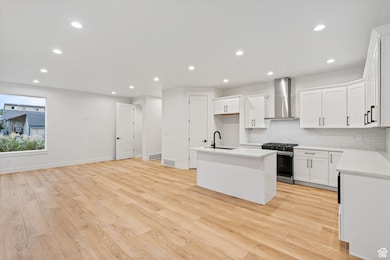 Kitchen featuring tasteful backsplash, gas range, white cabinets, wall chimney exhaust hood, and a kitchen island