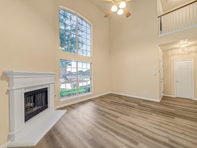 Unfurnished living room with a high ceiling, a fireplace with raised hearth, light wood-type flooring, and a ceiling fan