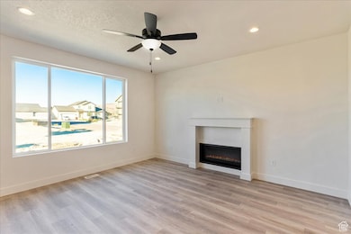 Unfurnished living room with light wood-style floors, recessed lighting, ceiling fan, a glass covered fireplace, and a residential view