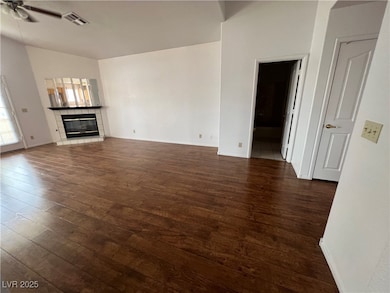 Unfurnished living room with a tiled fireplace, dark wood-type flooring, lofted ceiling, and ceiling fan