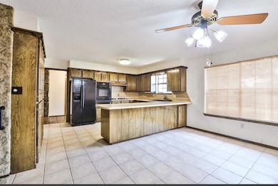 Kitchen with black refrigerator with ice dispenser, a peninsula, light countertops, a sink, and a ceiling fan