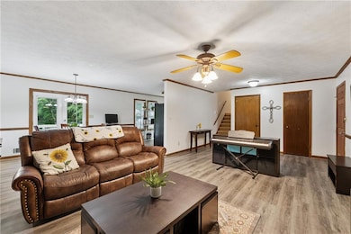Living area featuring stairway, baseboards, ceiling fan, light wood-style flooring, and a textured ceiling