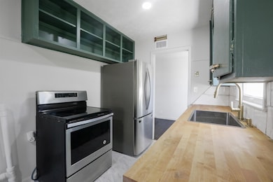 Kitchen with butcher block countertops, stainless steel appliances, open shelves, and green cabinetry
