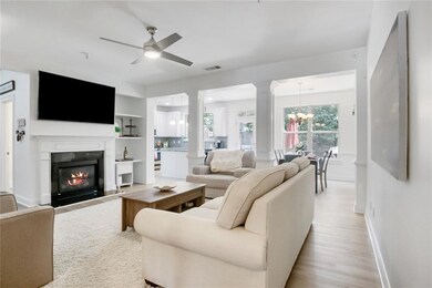 Living room with ornate columns, a ceiling fan, light wood-type flooring, a chandelier, and a fireplace with flush hearth