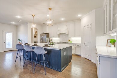 Kitchen with an island with sink, white cabinetry, light stone countertops, hanging light fixtures, and a breakfast bar area
