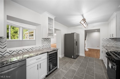 Main kitchen with tasteful backsplash, appliances with stainless steel finishes, white cabinets, and dark stone countertops