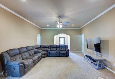 Carpeted living room with ceiling fan and crown mo