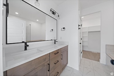 Bathroom featuring double vanity, a spacious closet, recessed lighting, light marble finish flooring, and a shower with door