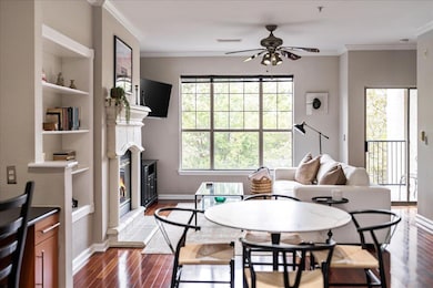 Living room with dark wood-style flooring, crown molding, a glass covered fireplace, ceiling fan, and built in features