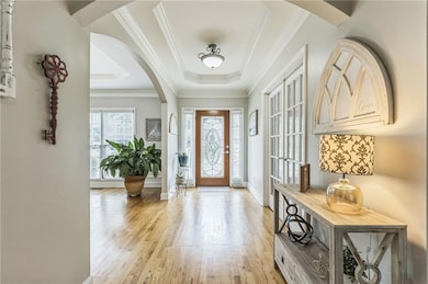 Entryway featuring a tray ceiling, light wood-type flooring, arched walkways, and crown molding