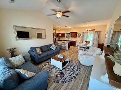 Living room featuring light wood finished floors, a chandelier, vaulted ceiling, and a ceiling fan