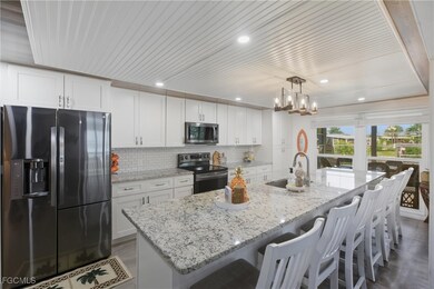Kitchen with appliances with stainless steel finishes, a kitchen breakfast bar, white cabinetry, light stone counters, and a kitchen island with sink