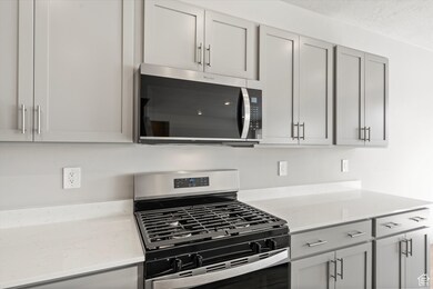 Kitchen with appliances with stainless steel finishes, light stone countertops, gray cabinets, and a textured ceiling