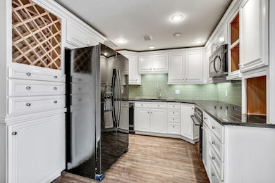 Kitchen with black appliances, white cabinets, ta