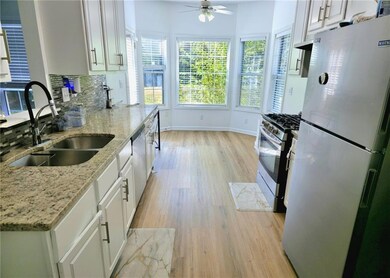 Kitchen featuring stainless steel appliances, white cabinetry, light stone counters, light wood-style floors, and tasteful backsplash