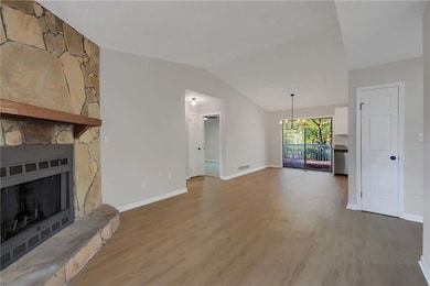 Unfurnished living room with light wood-type flooring, a fireplace, a chandelier, and vaulted ceiling