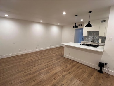 Kitchen with light countertops, white cabinetry, decorative backsplash, decorative light fixtures, and a peninsula