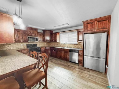 Kitchen featuring appliances with stainless steel finishes, decorative light fixtures, dark brown cabinets, light wood-style floors, and decorative backsplash
