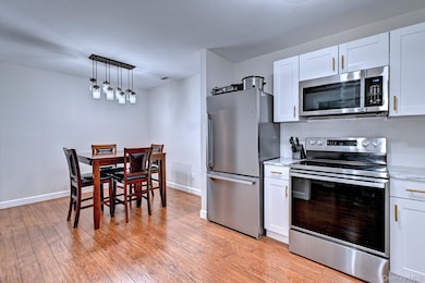 Kitchen featuring stainless steel appliances, white cabinetry, pendant lighting, and light wood-style floors